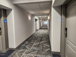 Un pasillo de hotel con alfombra estampada, paredes blancas y puertas con los números 224 y 225.