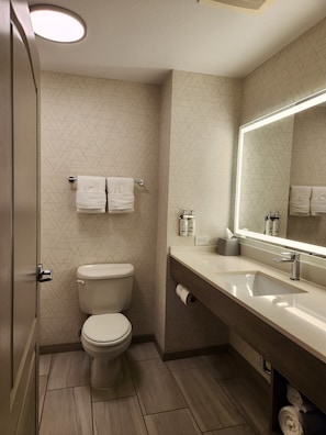 A modern bathroom with a toilet, a sink with a mirror, and patterned wall tiles. - Holiday Inn Express Hotel & Suites Crawfordsville by IHG (Crawfordsville)