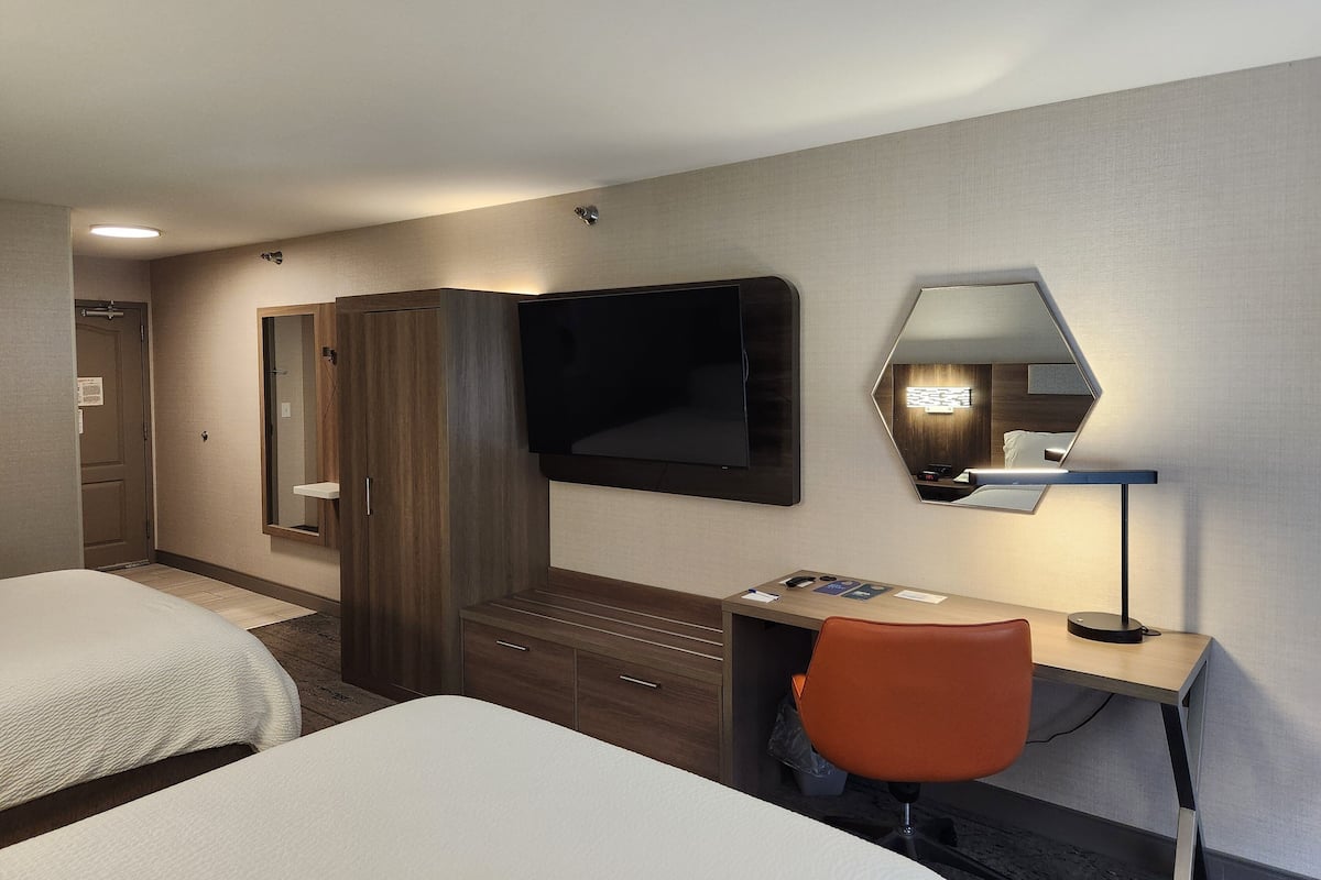 A hotel room with a bed, a desk, a chair, a TV, a wardrobe, and a mirror.