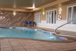 An indoor swimming pool with a no diving sign, blue chairs, and a lifebuoy on the wall.