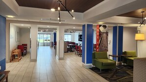 A spacious hotel lobby with a high ceiling, modern lighting fixtures, and a view of the dining area through a glass door. - Holiday Inn Express Hotel & Suites Crawfordsville by IHG (Crawfordsville)