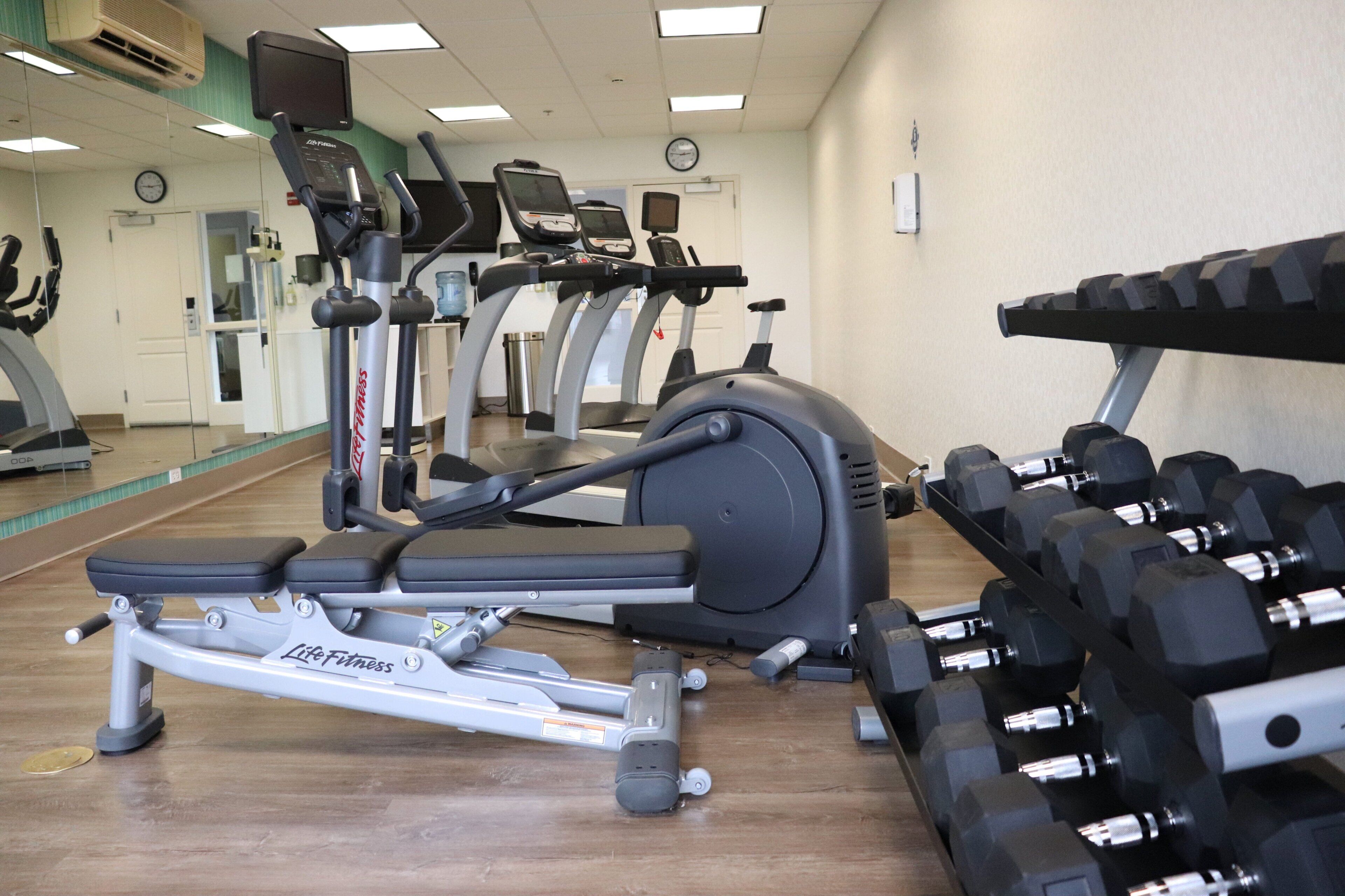 Une salle de sport équipée de matériel d’exercice, notamment des tapis de course, un vélo d’appartement et des haltères.