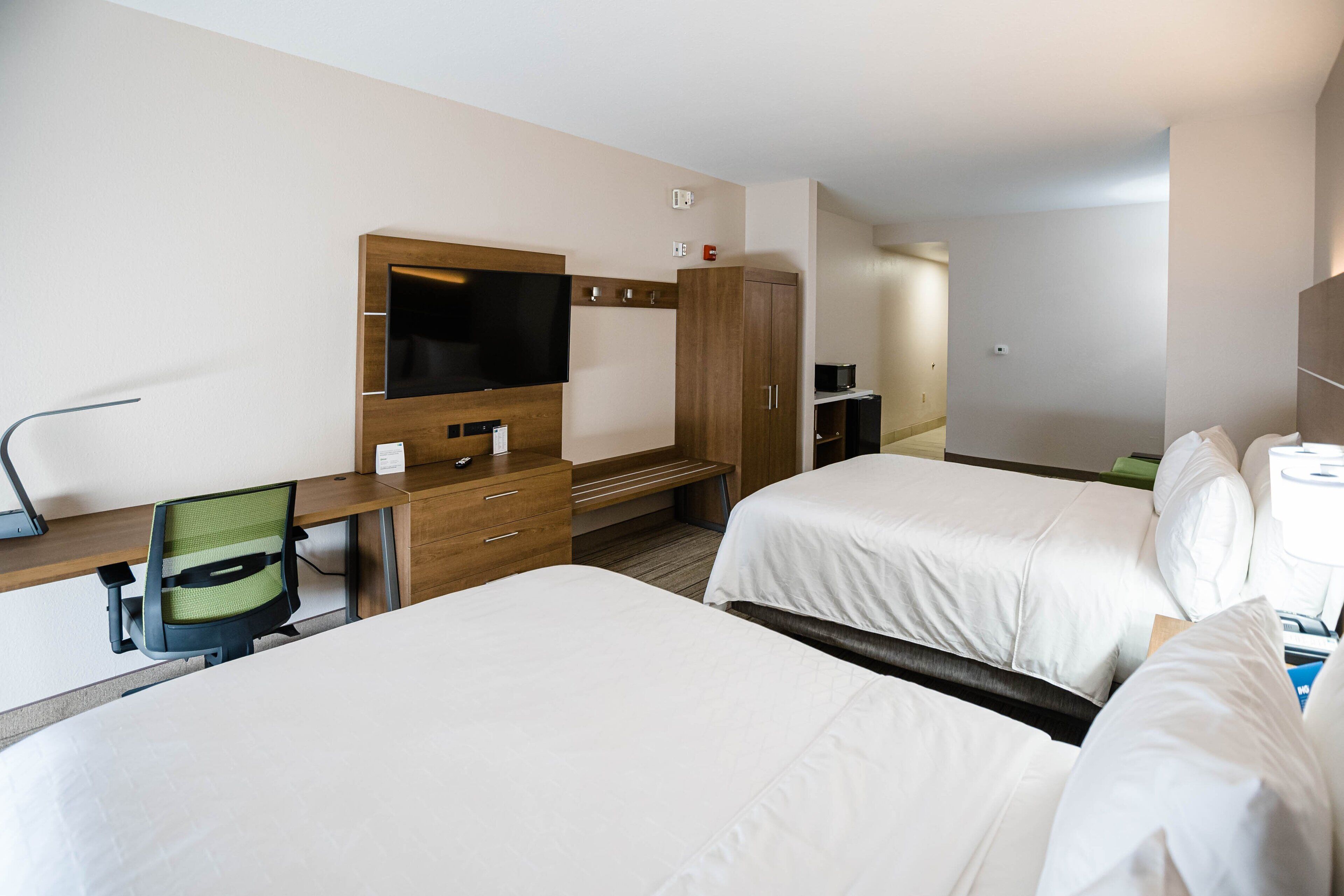 Una habitación de hotel con dos camas, un escritorio con silla, televisión y armario.