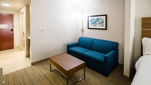 Habitación de hotel con sofá azul, una mesa de centro de madera, cama y paleta de colores enmarcada en la pared.