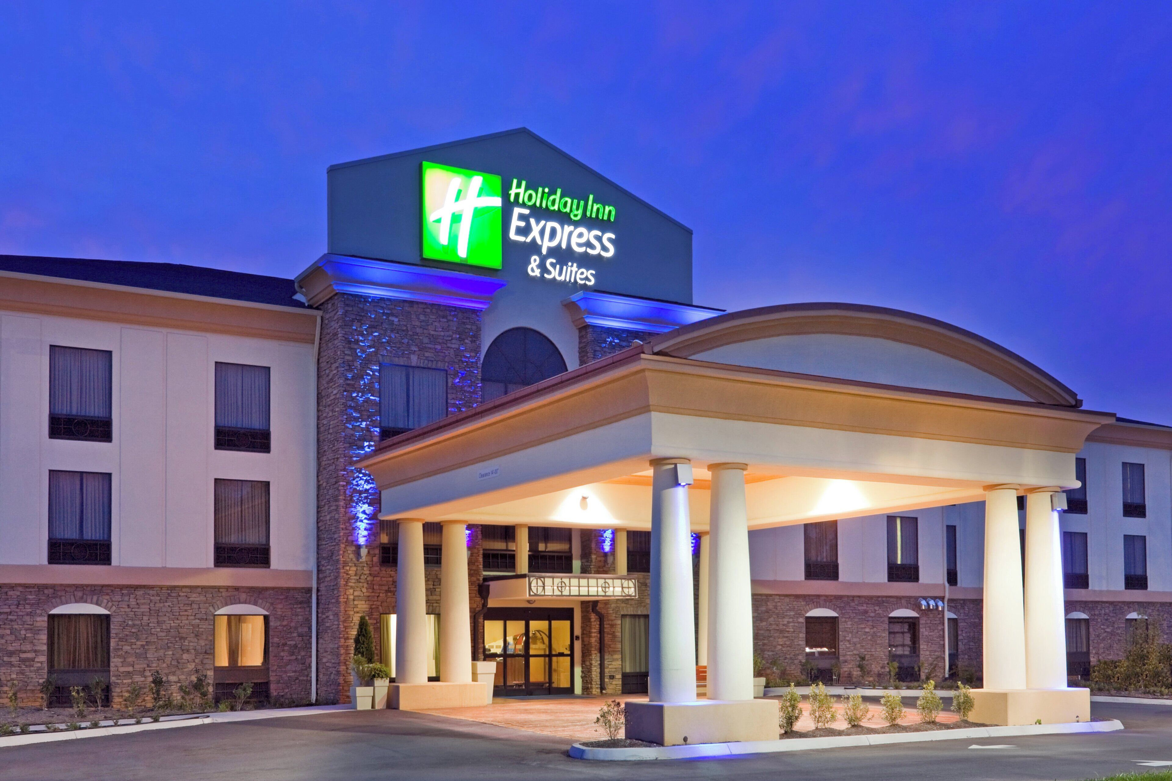 A Holiday Inn Express & Suites hotel with a prominent sign, a covered entrance, and a stone facade.