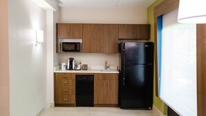 Una cocina compacta con armarios de madera, un refrigerador negro, un microondas y un lavavajillas.