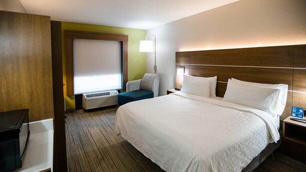 Una habitación de hotel con una cama grande, un escritorio, una silla y una ventana con persianas.