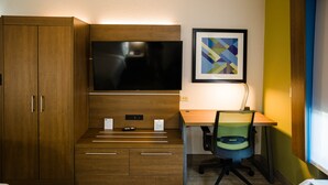 Habitación de hotel con un armario de madera, un televisor de pantalla plana sobre un escritorio, una silla y una obra de arte abstracto enmarcada en la pared.