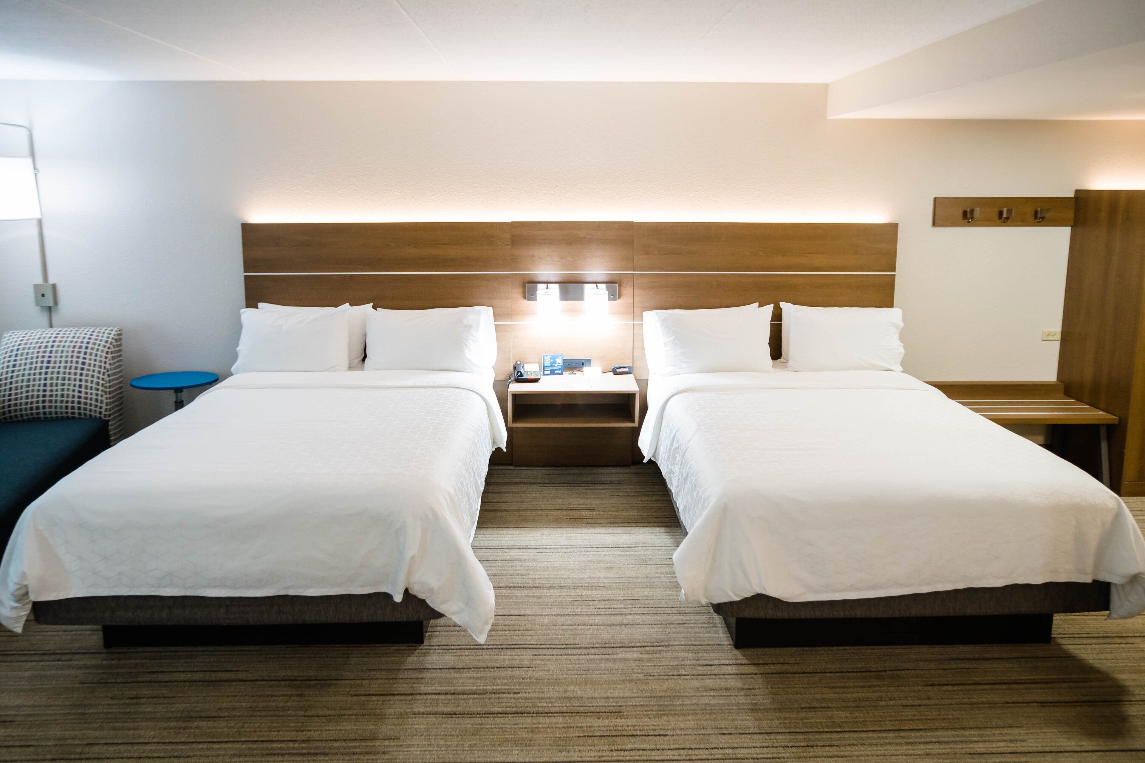 A hotel room with two beds, a nightstand, a lamp, and a wall-mounted mirror.