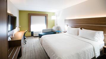 A hotel room with a large bed, a desk with a chair, a television, and a window with blinds.