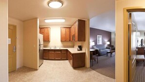 A compact kitchen with wooden cabinets, a refrigerator, and a coffee maker. There is a small dining area with a table and chairs. - Holiday Inn Express & Suites Willows by IHG (Willows)