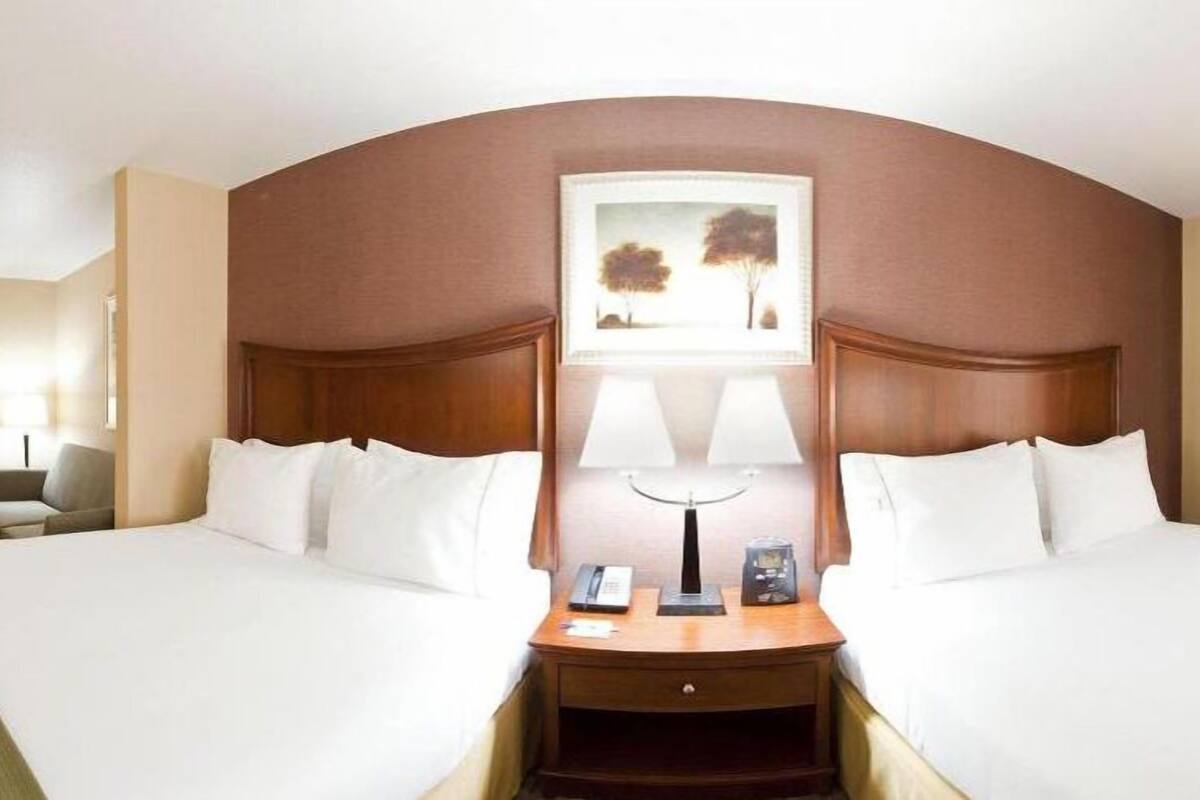 A hotel room with two beds, a nightstand with a lamp, a telephone, and a painting on the wall.