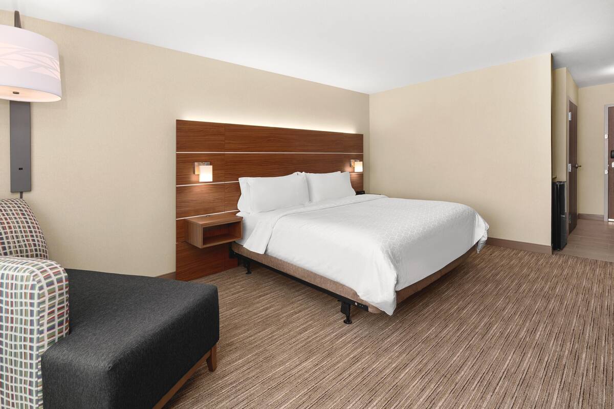 A hotel room with a bed, a desk, a chair, and a lamp.