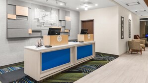 A reception area with a modern design, featuring a reception desk with a digital screen, a wooden counter, and a blue partition. There are framed pictures on the wall and a patterned carpet on the floor. - Holiday Inn Express & Suites Willows by IHG (Willows)