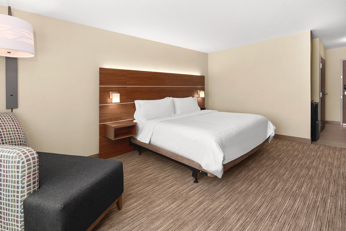 A hotel room with a bed, a desk, a chair, and a lamp.