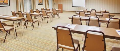 A conference room with multiple tables and chairs, a projector screen, and a carpeted floor.