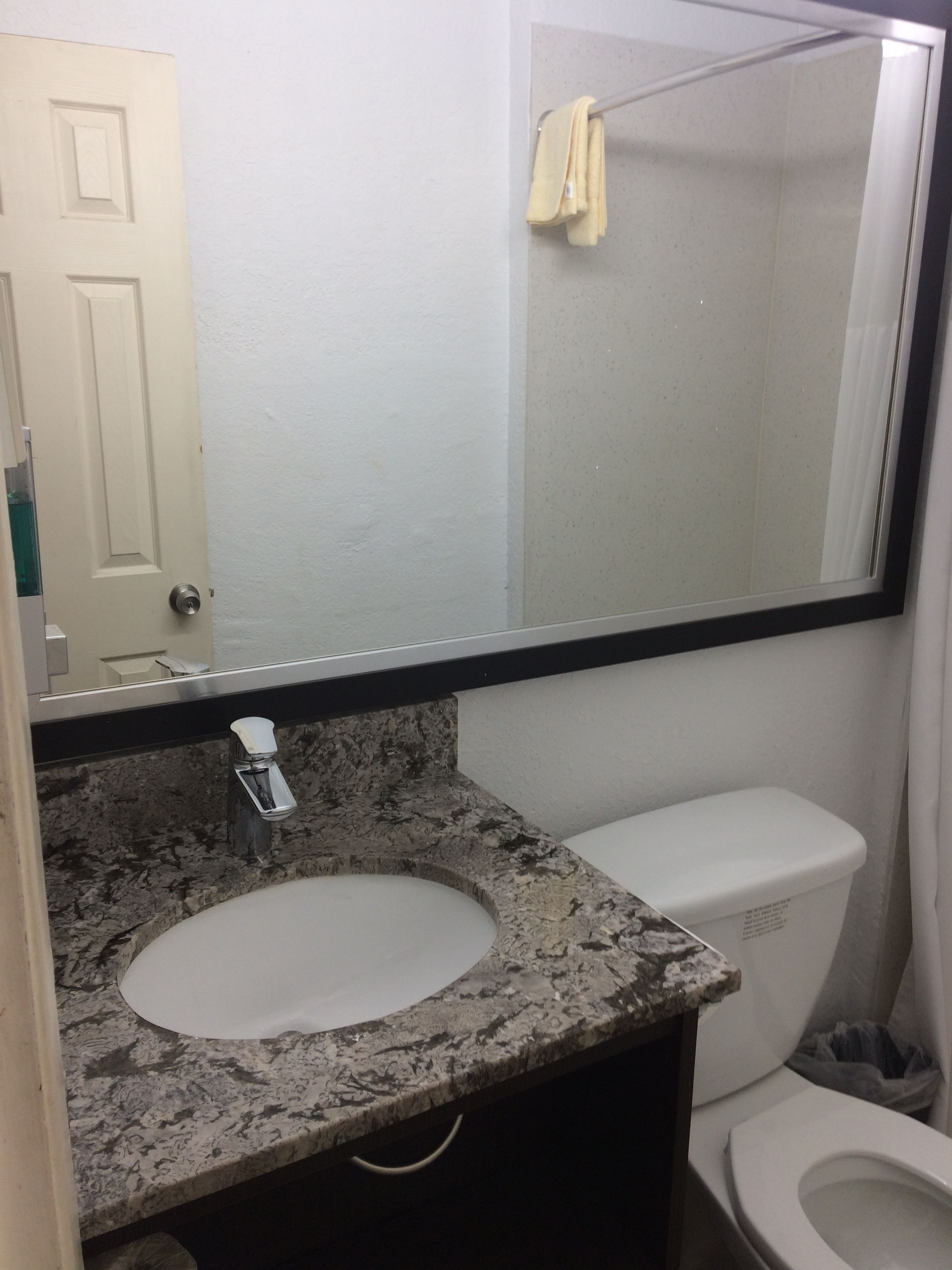 A bathroom with a granite countertop sink, a white toilet, and a mirror above the sink.