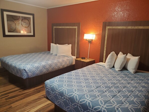 Habitación de hotel con dos camas, cada una con una colcha estampada y almohadas blancas. Hay una mesita de noche con una lámpara entre las camas.