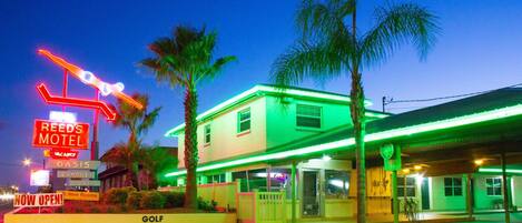 A motel with neon signage, a golf course sign, and a building with green lighting.