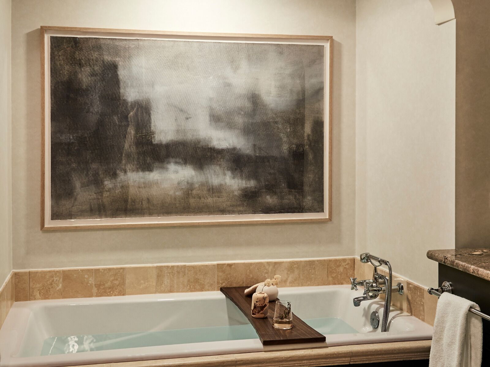 A bathroom with a large bathtub, a wooden tray with toiletries, and a large abstract painting on the wall.