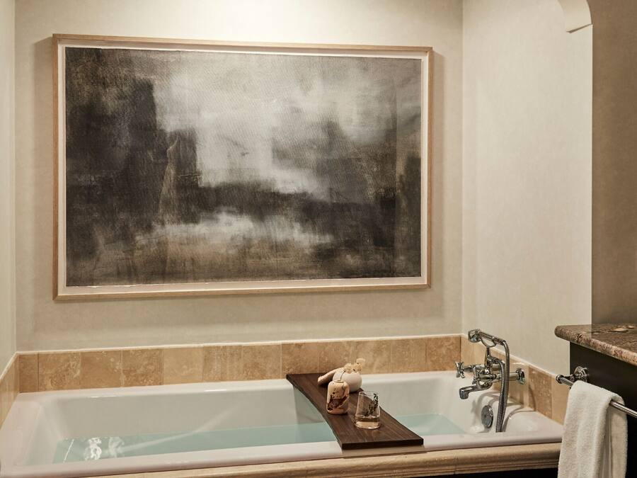 A bathroom with a large bathtub, a wooden tray with toiletries, and a large abstract painting on the wall.