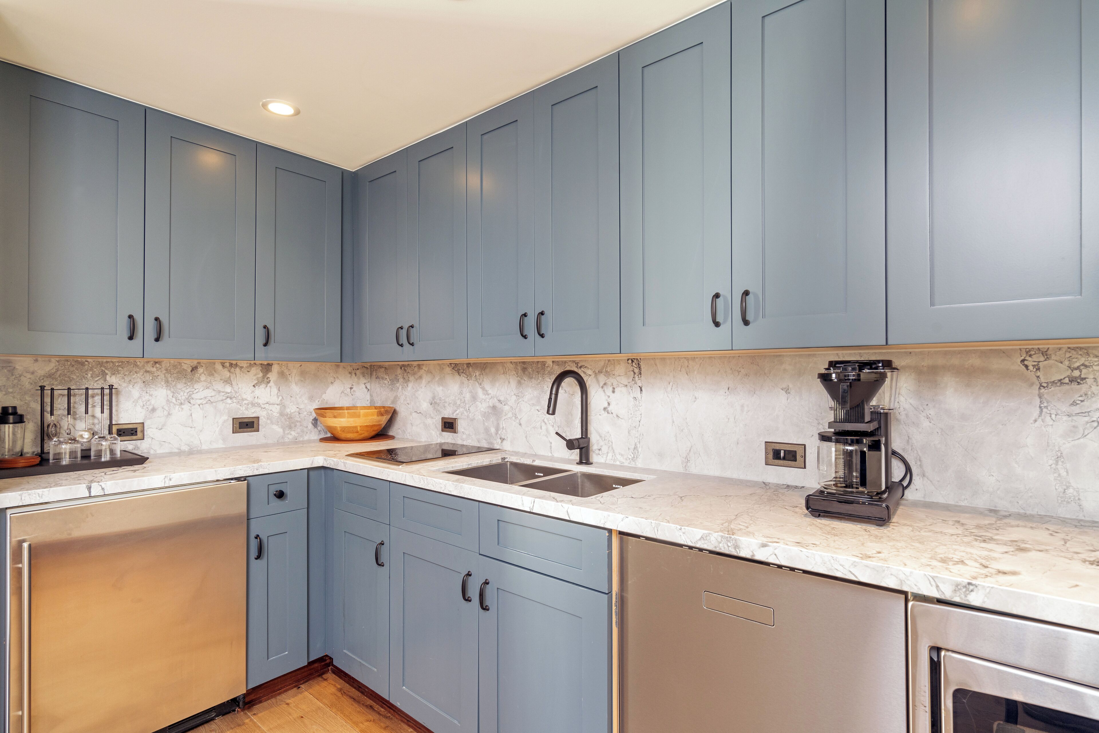 A kitchen with blue cabinets, a marble countertop, a sink, a coffee maker, and a dishwasher.