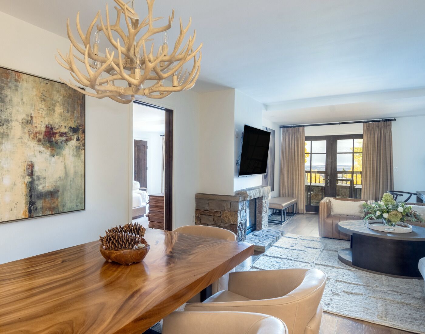 A modern living room with a wooden dining table, a stone fireplace, and a large window with curtains.
