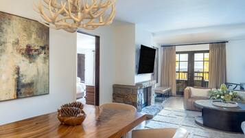A modern living room with a wooden dining table, a stone fireplace, and a large window with curtains.