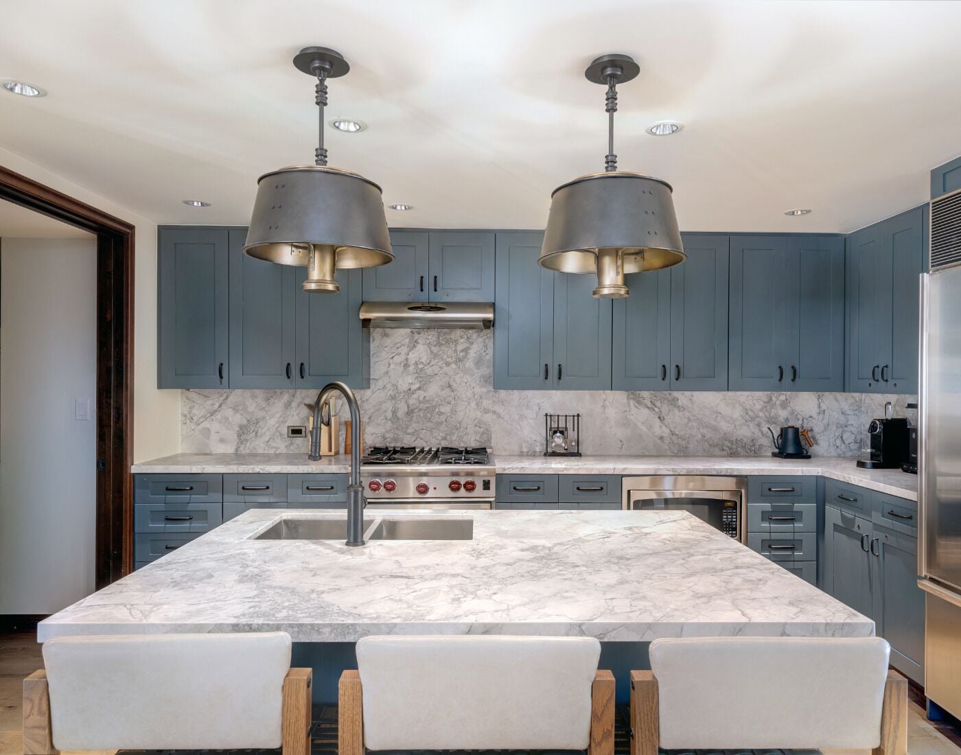 A modern kitchen with marble countertops, stainless steel appliances, and blue cabinetry.