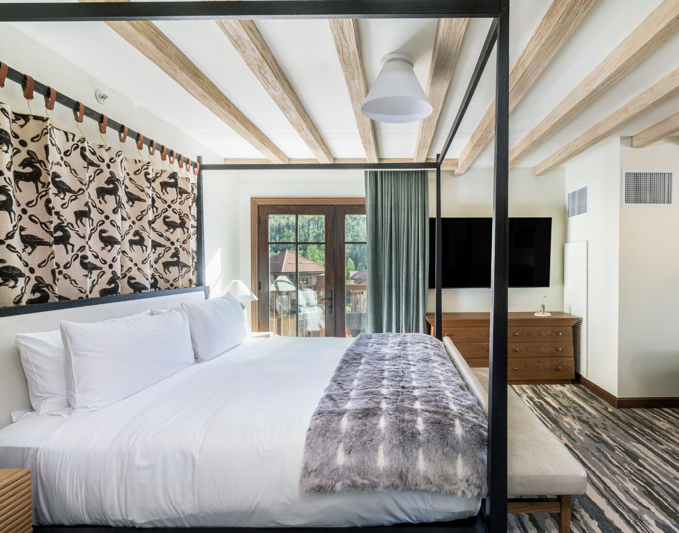 A modern hotel room with a large bed, a TV, a wooden headboard, and a balcony with a view of the outside.