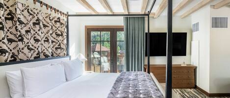 A modern hotel room with a large bed, a TV, a wooden headboard, and a balcony with a view of the outside.