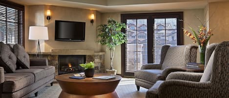 Una sala de estar con chimenea, televisor de pantalla plana y un ventanal con persianas.