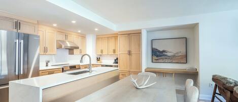 A modern kitchen with a central island, stainless steel appliances, wooden cabinets, and a dining area with a table and chairs.
