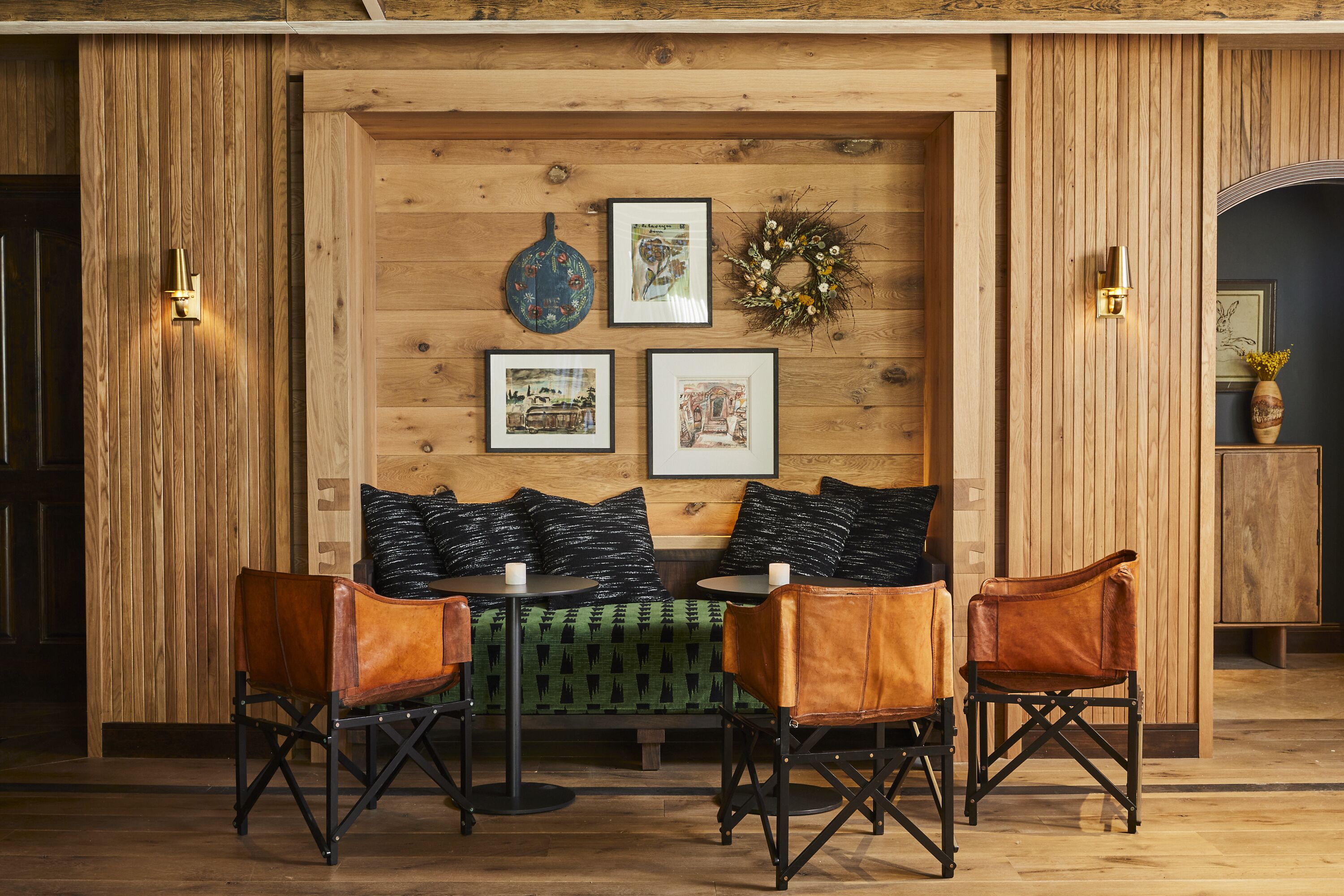 A cozy room with a wooden wall, a green patterned sofa, leather chairs, and framed pictures.