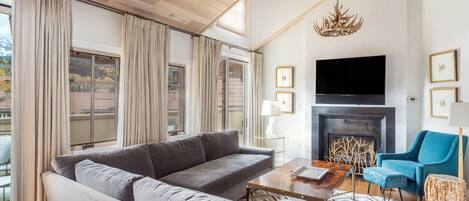 A spacious living room with a grey sectional sofa, a coffee table, a blue armchair, and a fireplace.