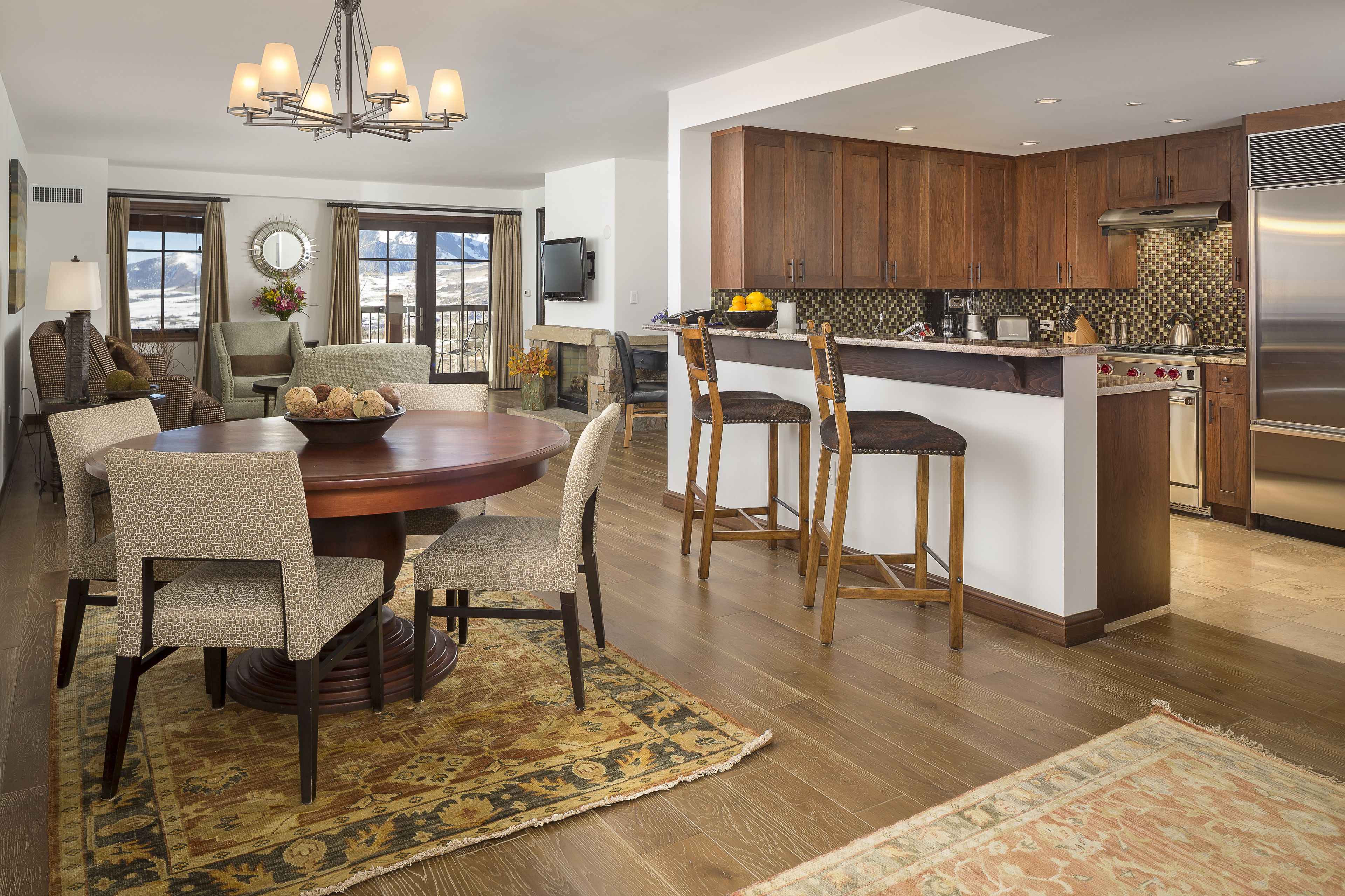 A modern kitchen with wooden cabinets, a stainless steel refrigerator, and a dining area with a round table and chairs.