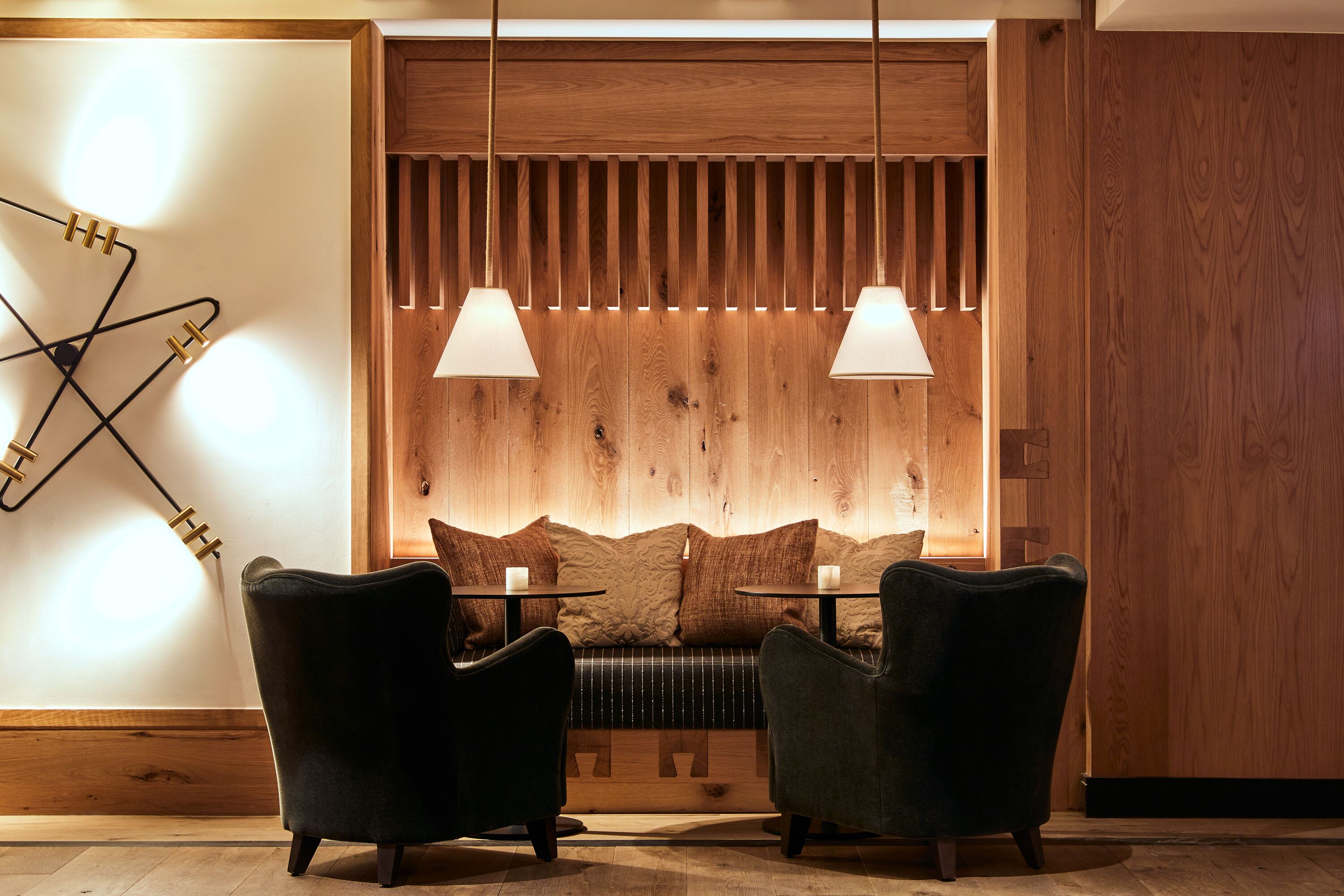 Un interior moderno con una pared de acento de madera, dos sillones tapizados, un banco e iluminación colgante.