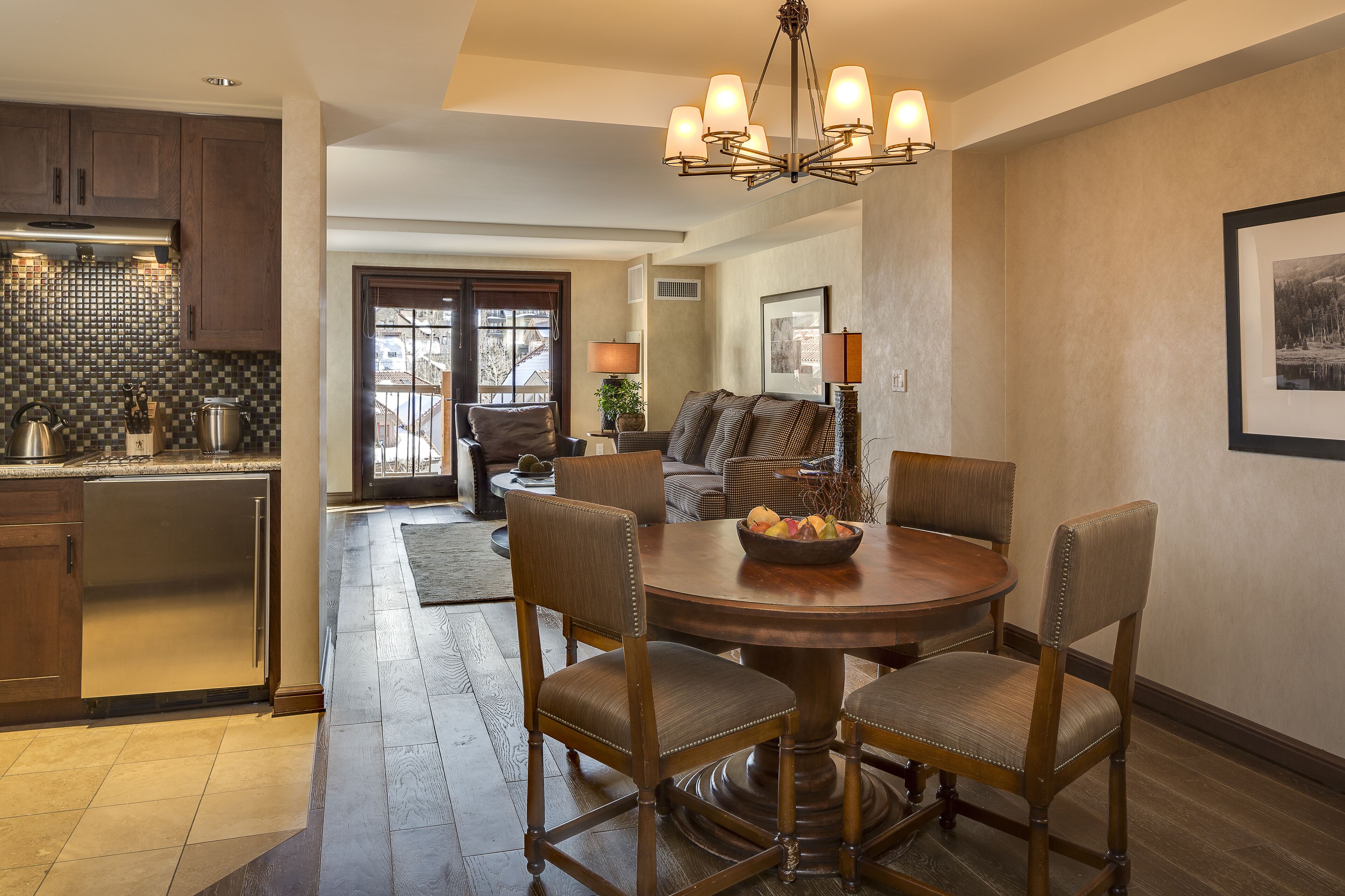 A dining area with a round wooden table, four upholstered chairs, and a chandelier.