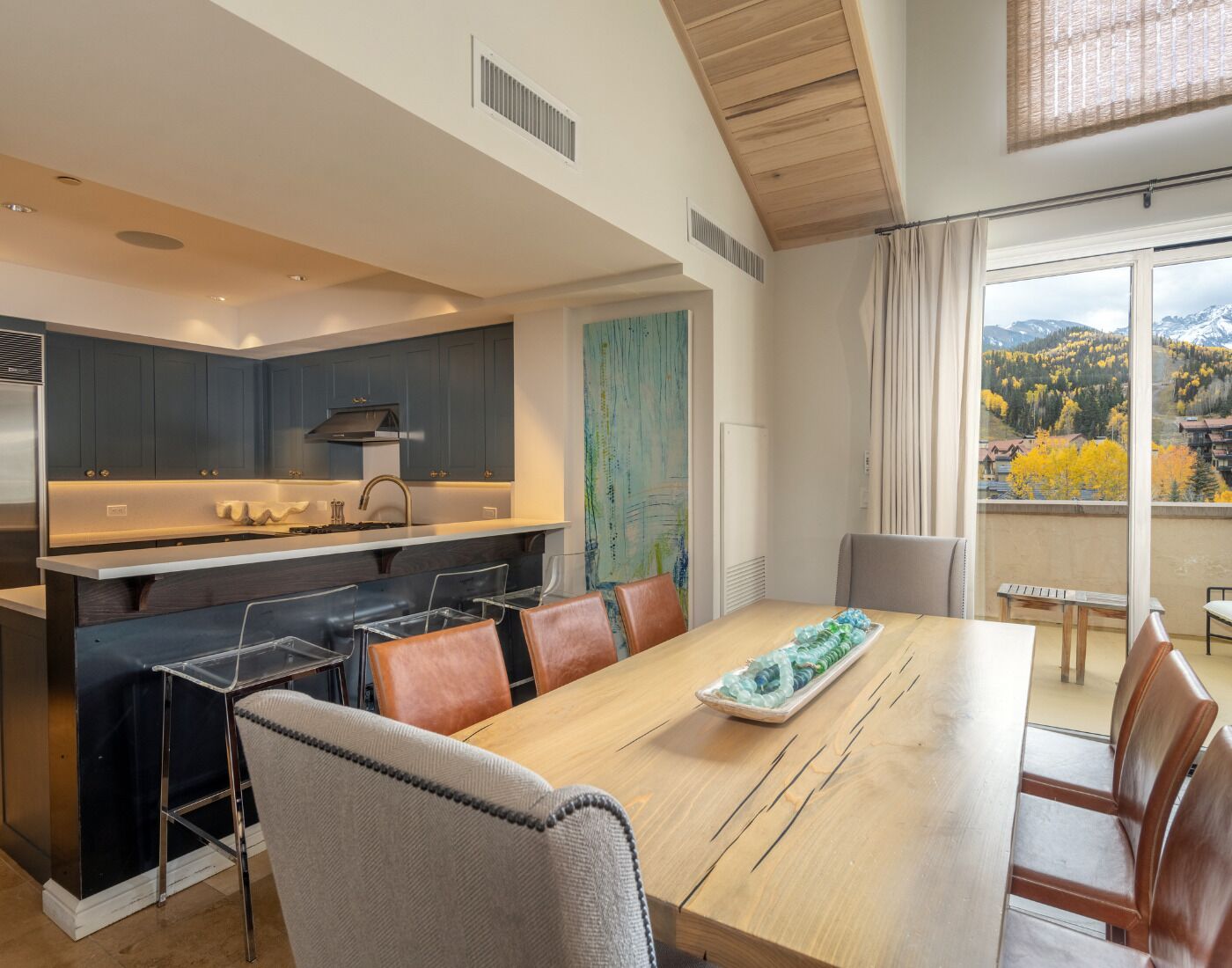 A modern kitchen with dark cabinets, a central island, and a dining area with a wooden table and chairs.