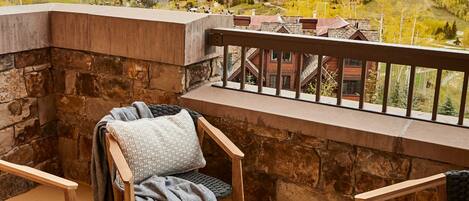 Un balcón con paredes de piedra, muebles de madera y vistas a un paisaje montañoso.