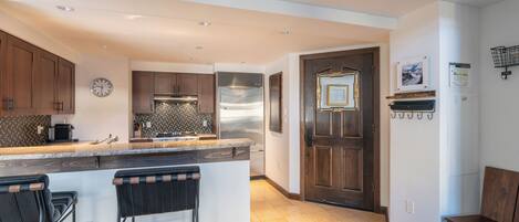 A modern kitchen with a central island, bar stools, wooden cabinets, and a stainless steel refrigerator.