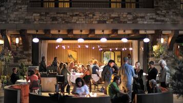 An outdoor dining area with stone walls and hanging lights. Tables are set for dining, and people are seated.