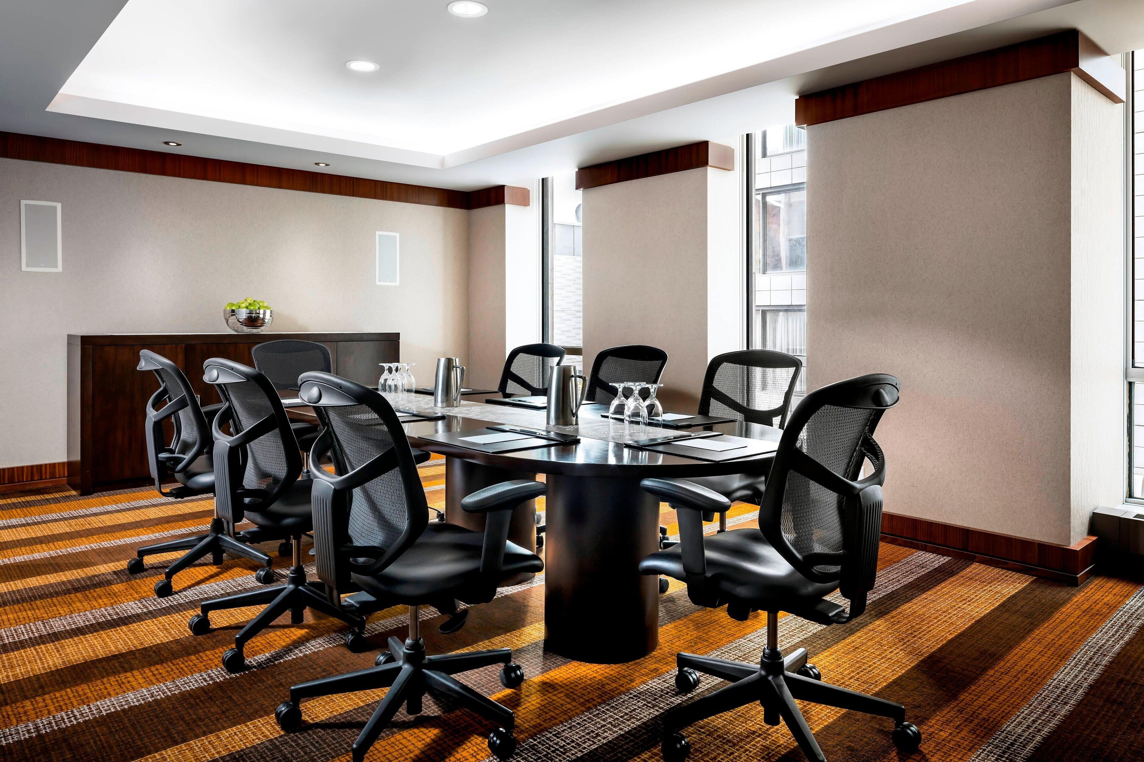 A conference room with a large table, six black office chairs, a coffee station, and a plant on the wall.