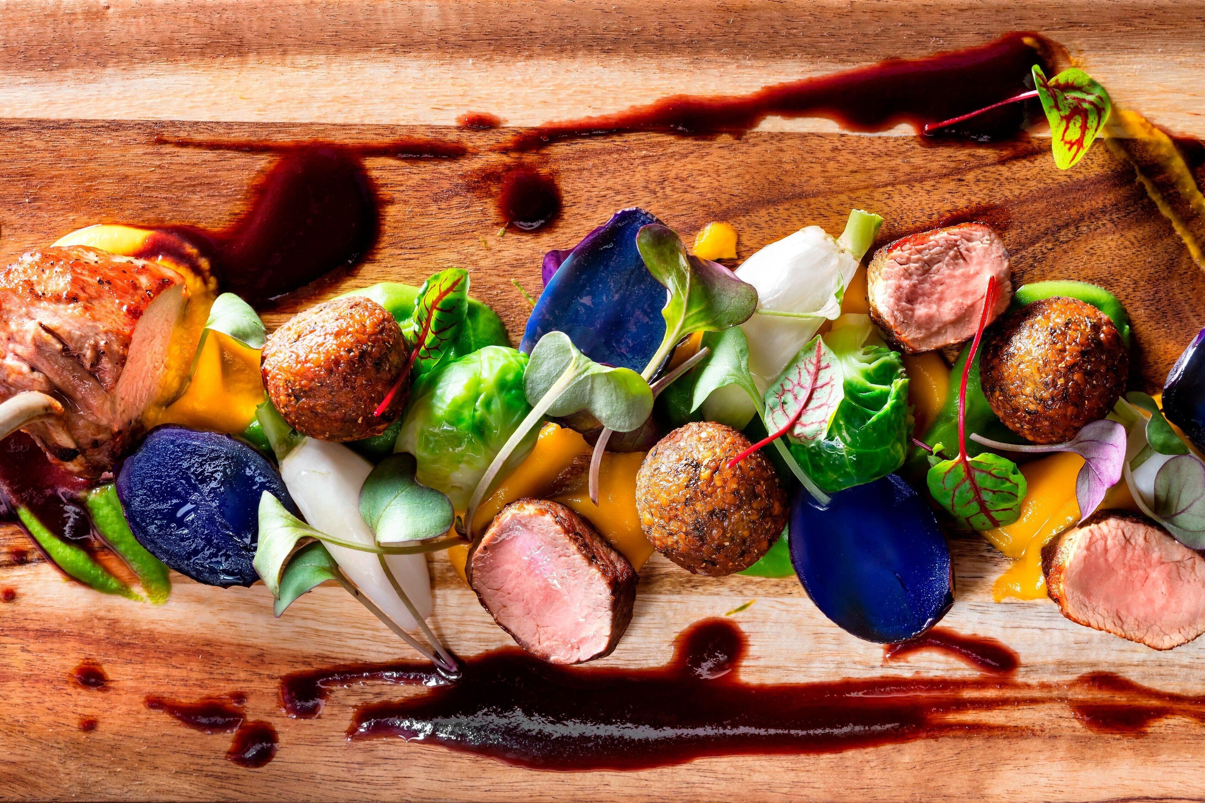 A wooden table with a variety of food items including meat, vegetables, and garnishes.