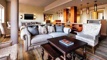 A modern hotel room with a large sectional sofa, a small table, and a patterned armchair.