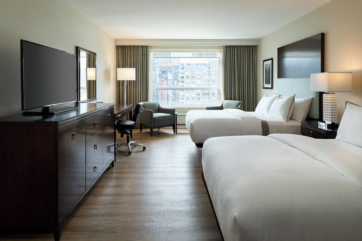 A hotel room with two beds, a TV, a desk, and a chair.