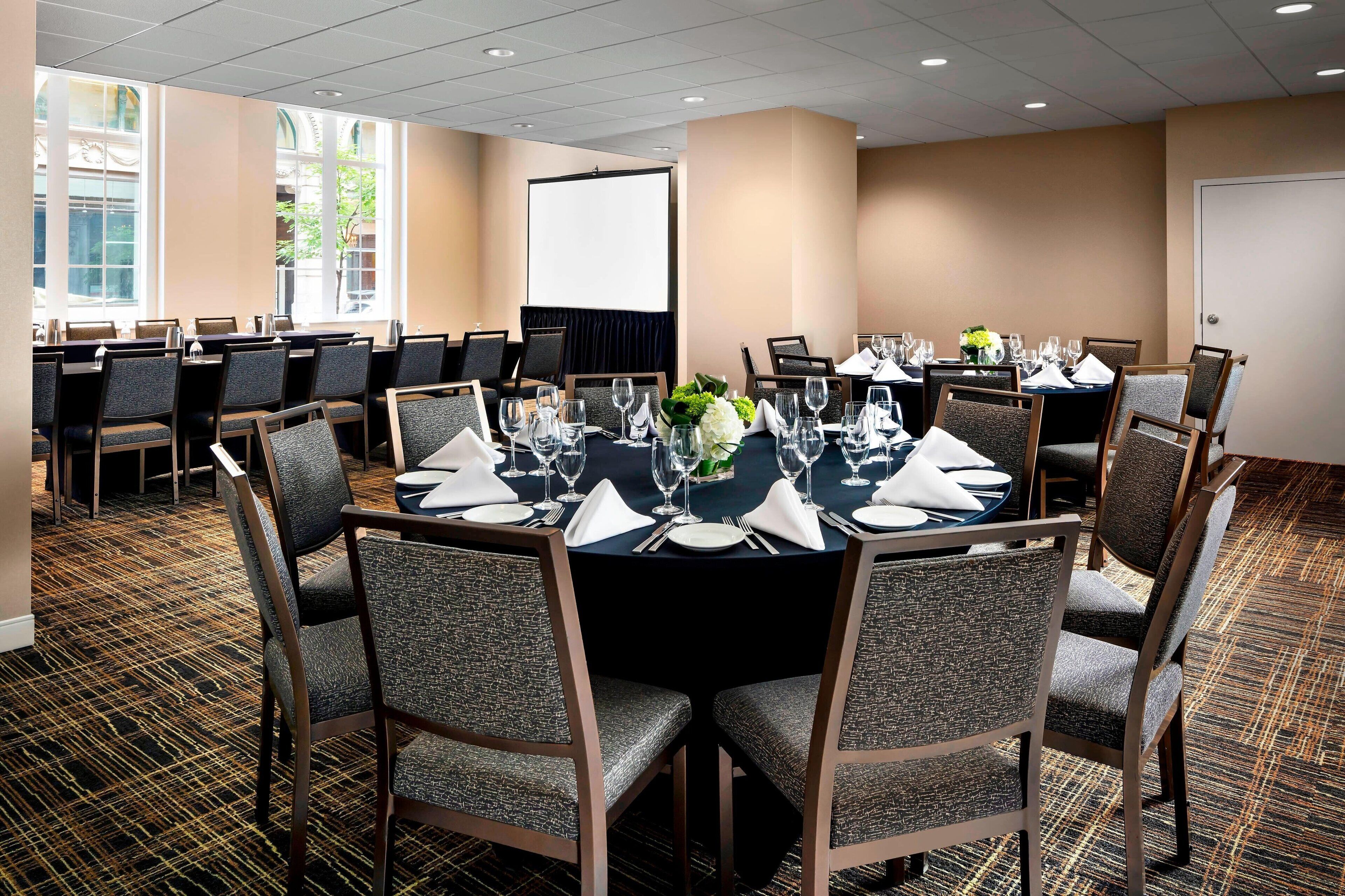 A conference room with round tables set for dining, equipped with chairs, tables, and a projector screen.