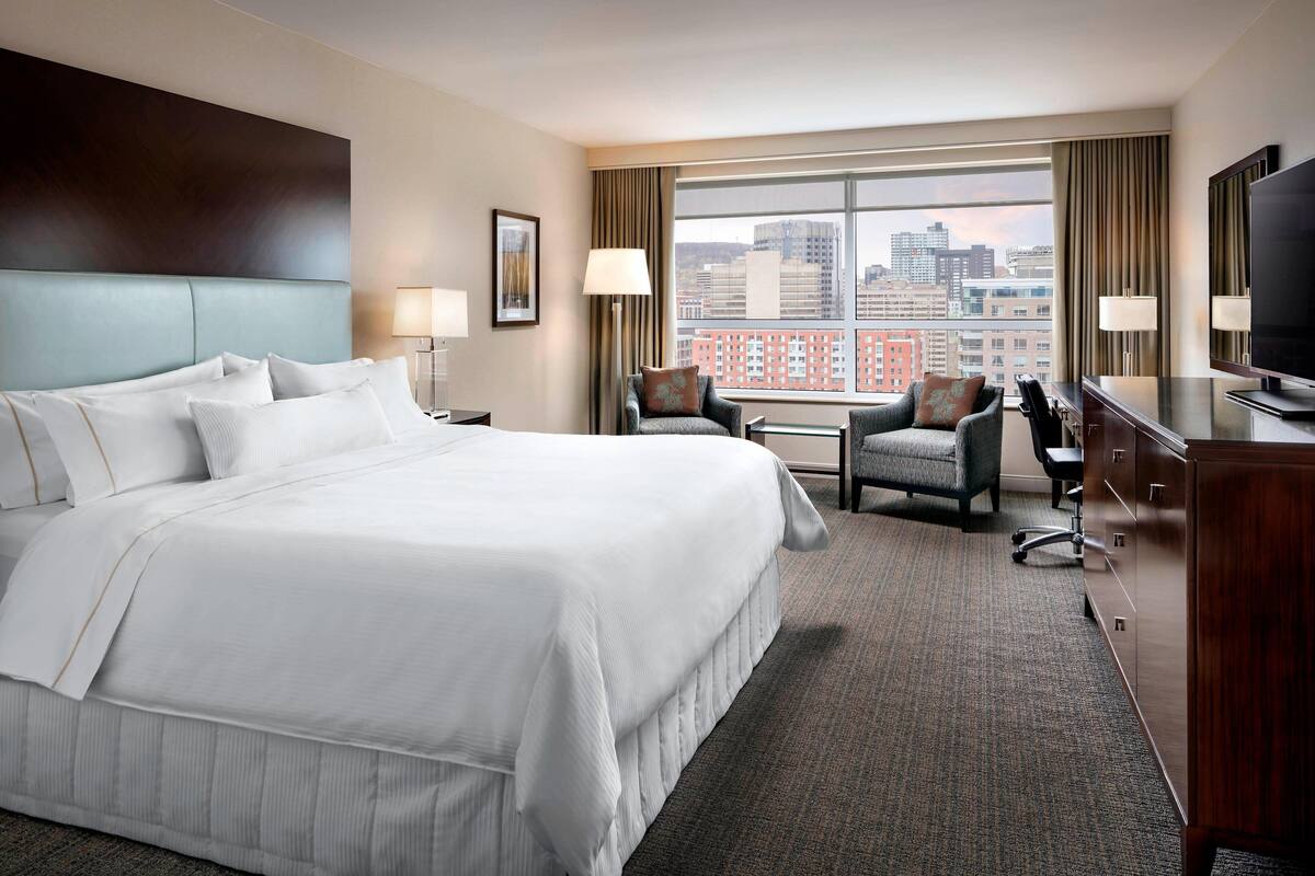 A hotel room with a large bed, two armchairs, a desk, and a TV.