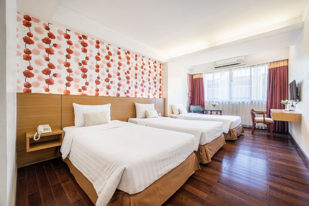 Hotellihuone, jossa on kolme sänkyä, puinen pääty, puhelin, työpöytä tuolilla ja televisio.