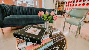 Un'area lounge moderna con un divano verde scuro, un tavolino rotondo con libri e un vaso di fiori, e una parete a motivi rossi e bianchi.